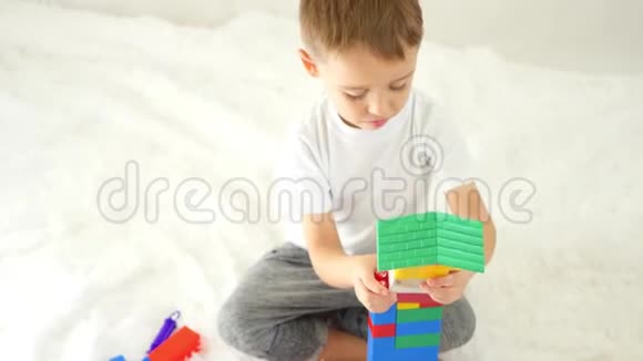 孩子在白色的背景上建造一座彩色积木的房子快乐男孩在玩儿童发展的概念视频的预览图