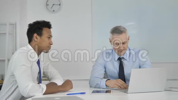 白发苍苍的商人在与非洲商人的笔记本电脑会议上讲解项目视频的预览图
