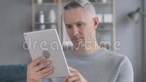 兴奋的白发男子在平板电脑上在线获奖视频的预览图
