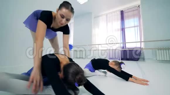 女芭蕾舞老师正在帮助小女孩伸展身体视频的预览图