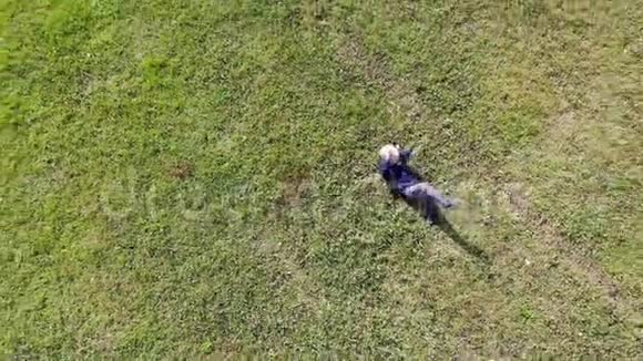 鸟瞰一个白人或西班牙裔男子躺在绿色草地上的阳光明媚的一天轻松的空中体验视频的预览图