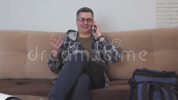 一名中年男子坐在酒店房间的沙发上正在打电话旁边是一个蓝色的旅游背包视频的预览图