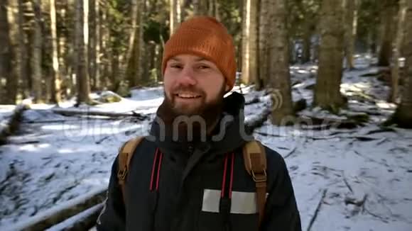 一个长着大胡子笑着的年轻人背着背包站在针叶林中的画像视频的预览图