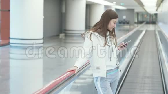 穿着运动服的漂亮女孩在机场的走道上使用电话视频的预览图