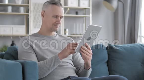 白发男坐在沙发上用平板电脑浏览互联网视频的预览图