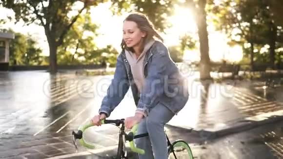 快乐微笑的女自行车骑手早上在城市街道或公园骑自行车背景上的镜头耀斑视频的预览图