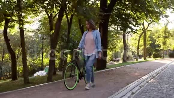 早晨公园里除了一辆自行车外还有一个年轻快乐的女人在前面散步带着她徒步行走的女孩视频的预览图