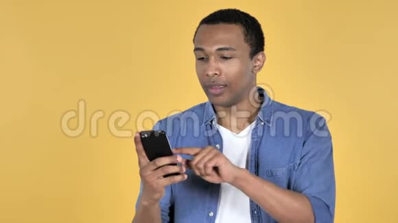 非洲年轻人浏览智能手机黄色背景视频的预览图