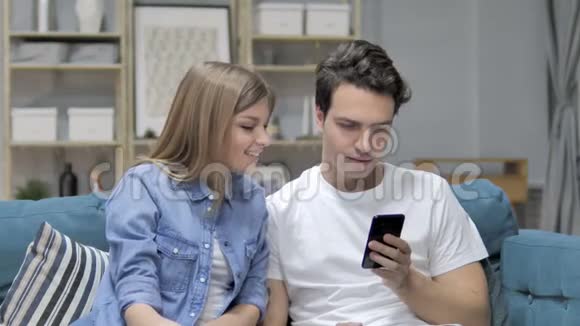 年轻夫妇在沙发上放松时使用智能手机传递信息视频的预览图