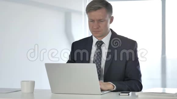 头痛穿着的商人在笔记本电脑上工作视频的预览图