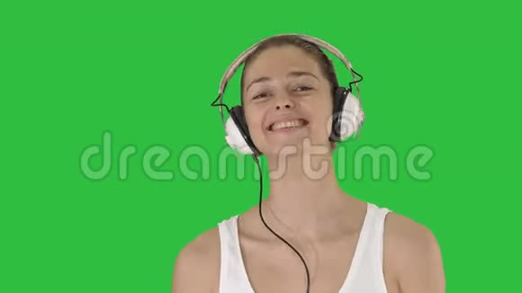 音乐人与科技理念幸福微笑的女人带着耳机走在绿色的屏幕上色度键视频的预览图