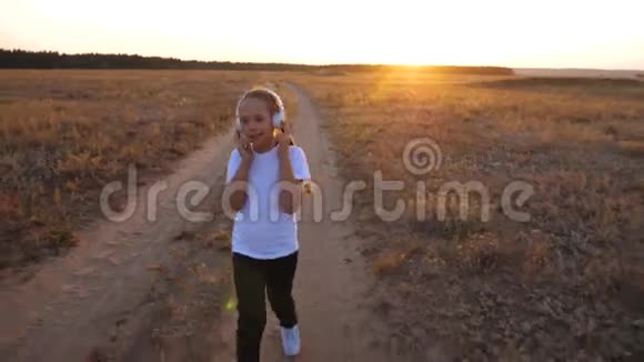 在城外日落时慢跑年轻女孩穿着白色T恤在日落时训练听音乐视频的预览图