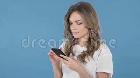 蓝色背景下的年轻女孩智能手机视频的预览图