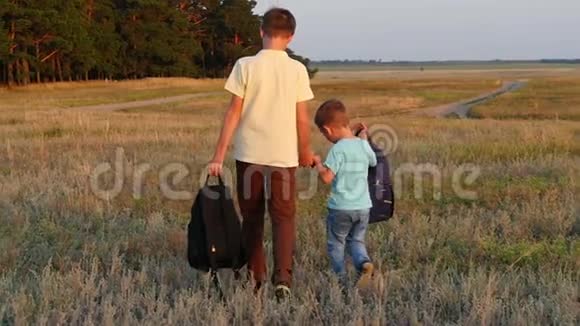 两个游客兄弟在日落时背着背包散步快乐的孩子走在大自然中靠近森林视频的预览图
