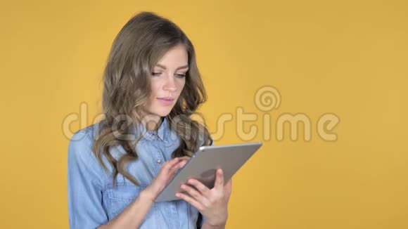 年轻女孩为成功而兴奋同时使用黄色背景下的平板电脑视频的预览图