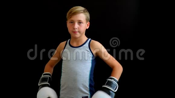 一个年轻的运动员站在黑暗的背景上男孩穿着灰色T恤双手戴手套黑白的视频的预览图