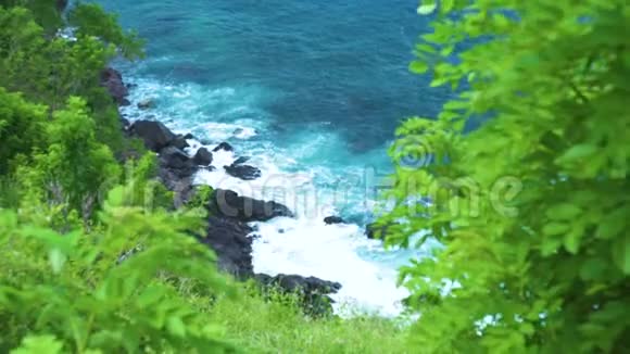 海浪破碎到岩石悬崖与喷雾和白色泡沫绿色植物的背景海浪拍打着岩石视频的预览图