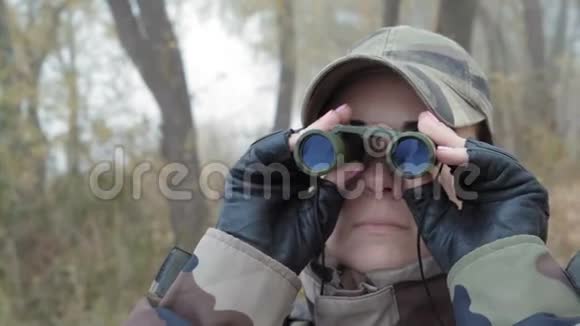 特写镜头身穿军服的美女一边站在河岸边一边用双筒望远镜看着邻居视频的预览图