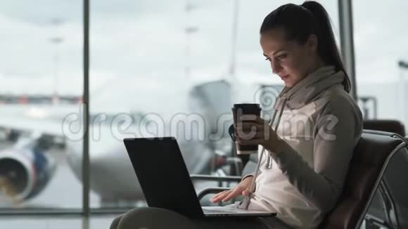 女自由职业者喝外卖咖啡用笔记本电脑在机场候机室工作视频的预览图