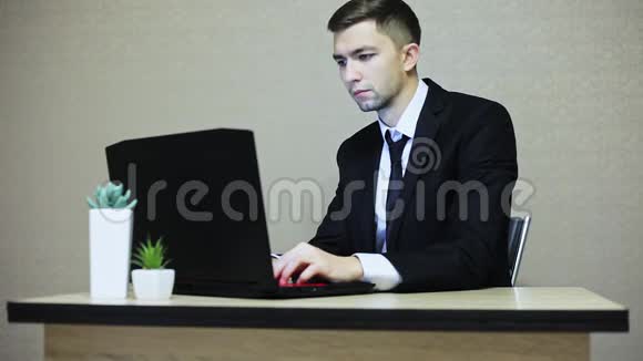 商人非常惊讶一边看着相机一边在办公室的笔记本电脑上工作视频的预览图