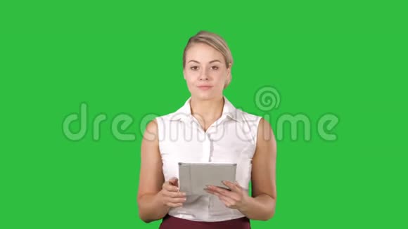 美丽的女孩拿着一个平板电脑触摸板电脑小玩意在绿色屏幕上看着相机色度视频的预览图