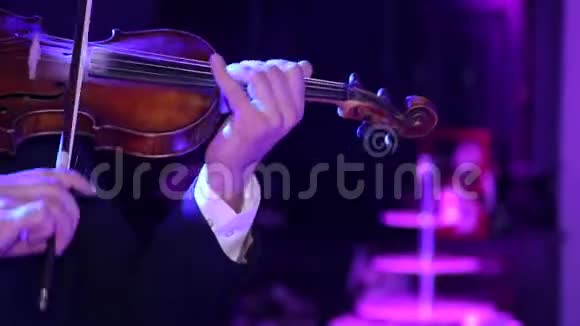特写男音乐家拉小提琴在黑暗的背景与彩色的灯光视频的预览图