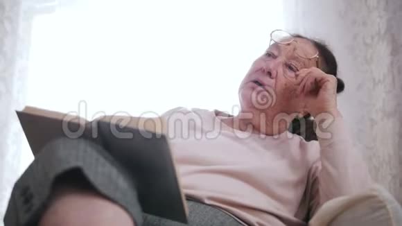 一位老妇人坐在窗户背景上的椅子和衣柜里视频的预览图