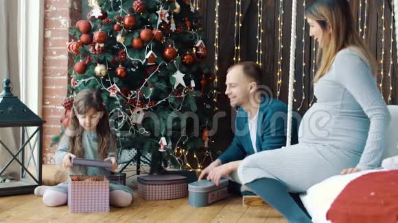 小女孩爸爸和怀孕的妈妈在圣诞树附近视频的预览图