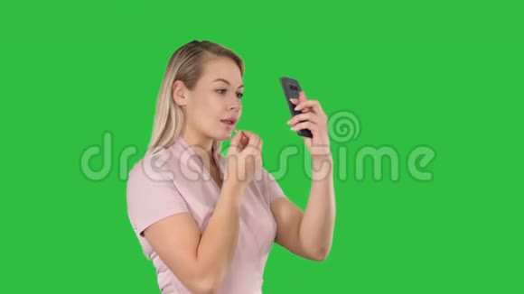 美女人化妆年轻的女人嘴唇看着绿色屏幕上的智能手机Chroma键视频的预览图