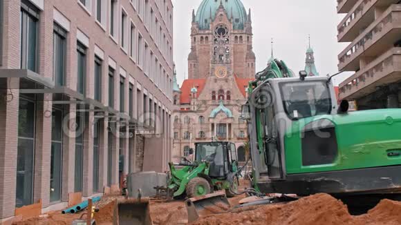在路上工作一台绿色大挖掘机在市政厅旁边修理道路中心有一个大钟慢慢视频的预览图