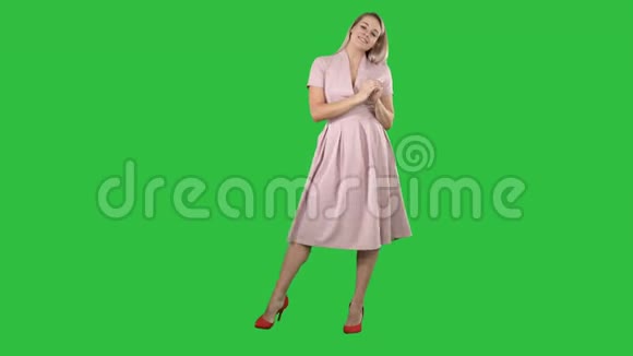 快乐的金发女人穿着粉红色与相机交谈并指向一个绿色屏幕的侧面Chroma键视频的预览图