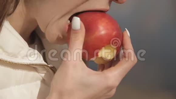 美丽的年轻女孩在公园里的一棵树下吃一个红苹果在水边看书嘴唇的特写视频的预览图