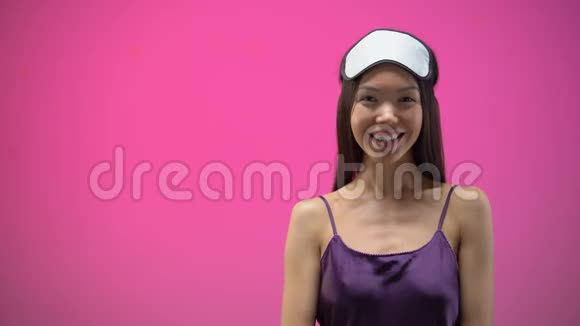 穿着睡衣戴着眼罩吹着纸屑的亚洲女孩被隔离在粉红色的背景上视频的预览图