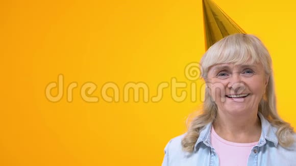 欢乐的祖母戴着派对帽在黄色背景上展示橙色气球视频的预览图