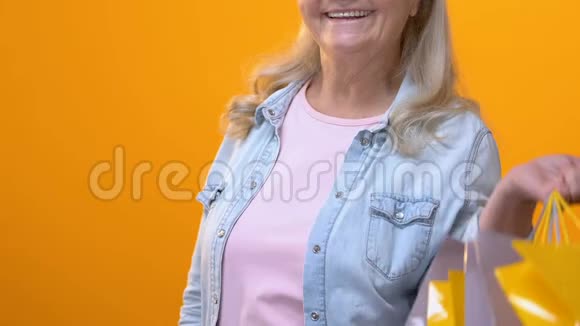 带着购物袋黄色背景的金卡的快乐退休女士视频的预览图