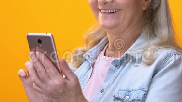 老妇人滚动智能手机应用程序和微笑相机社交网络视频的预览图