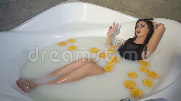 一个穿着黑色泳衣的性感女孩躺在浴室里牛奶和橘子视频的预览图