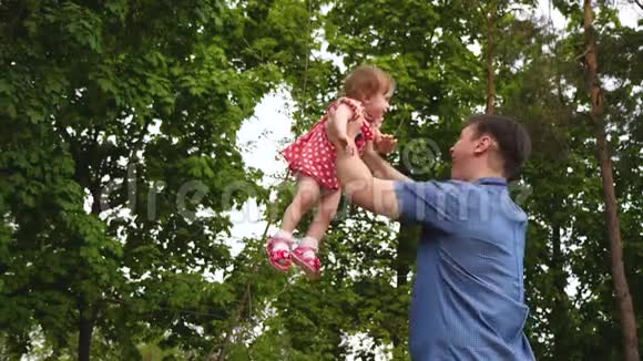 快乐爸爸正在温暖的绿色公园里空中盘旋小笑女儿父母在大自然中与婴儿玩耍周末视频的预览图