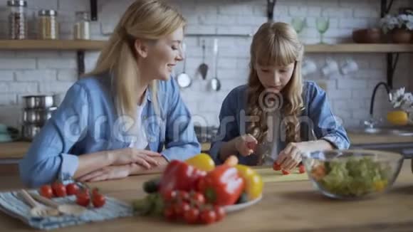 妈妈和女儿一起在一个明亮的大厨房做饭女孩帮妈妈切蔬菜视频的预览图