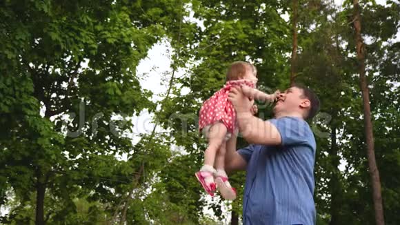 小女孩正笑着在爸爸怀里的空中飞翔做父亲的快乐儿童和家长在公园散步视频的预览图