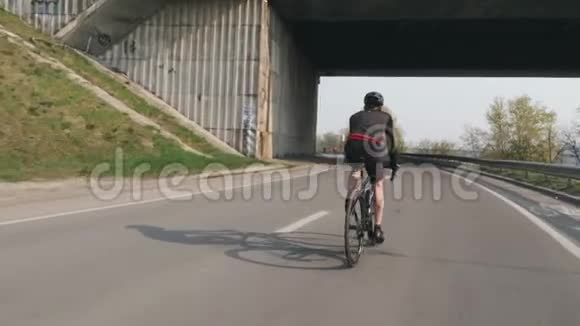 年轻健康的骑自行车的人骑在桥下自行车训练比赛男性骑自行车的人穿着黑色的衣服和头盔视频的预览图