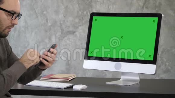 迷人的胡须男检查他的牙齿在他的手机自拍相机附近的电脑显示器绿色屏幕模拟显示视频的预览图