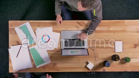 两个商人坐在木制桌面上处理文件和usina笔记本电脑视频的预览图