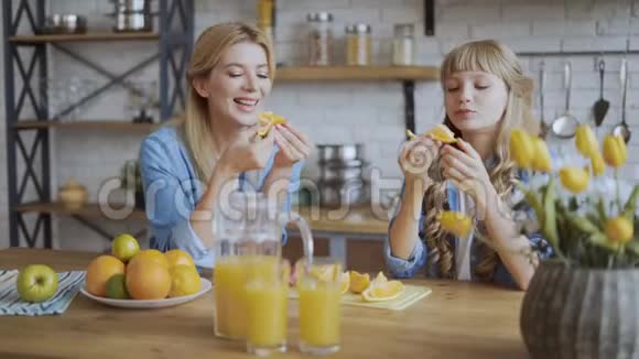 妈妈和女儿坐在餐厅里吃橘子多汁熟橙和幸福的家庭观念4K视频的预览图