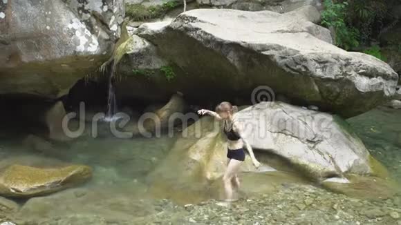 美丽的姑娘来到绿色的热带森林中沿着山下的小瀑布上面有巨石和苔藓视频的预览图