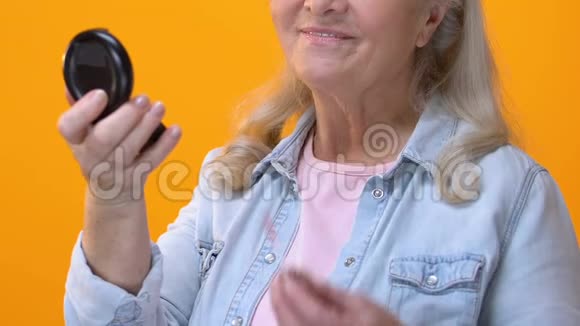 老年妇女在小镜子前涂抹唇彩抗衰老化妆品视频的预览图