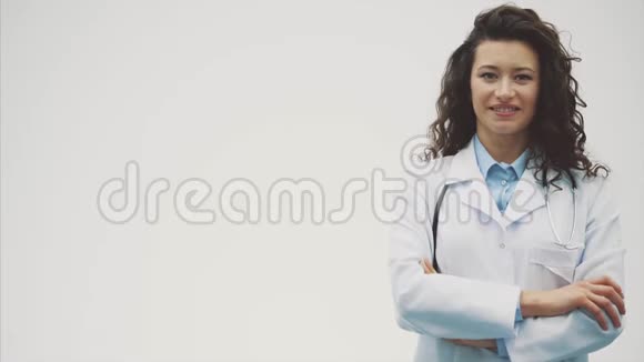 幸福的年轻微笑女孩医生的肖像穿着白色长袍在灰色背景上均匀交叉的双手视频的预览图