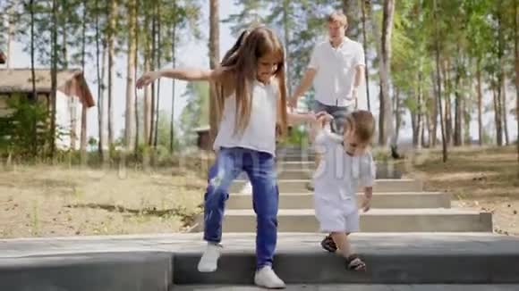 小女孩牵着小弟弟的手白天一起走在公园的石阶上父母是视频的预览图