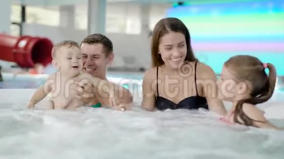 有两个小孩的幸福家庭正坐在一个游泳池里游泳坐在一小碗按摩浴缸里视频的预览图