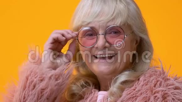 幸福的老太太戴着时髦的眼镜在明亮的背景下眨眼调情视频的预览图